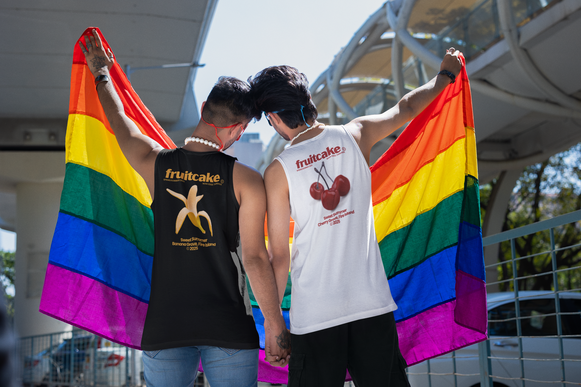 two Desi men in tanktops holding a rainbow pride flag and holding hands for gay pride with fruitcake banana and cherry tanks on