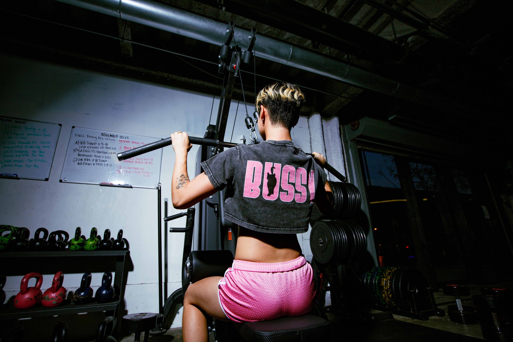 non-binary Person at the gym exercising and wearing a snow wash crop top with 'BUSSY' on the back with a Cat for BUSSY Cat Club series by Nova Edge Threads
