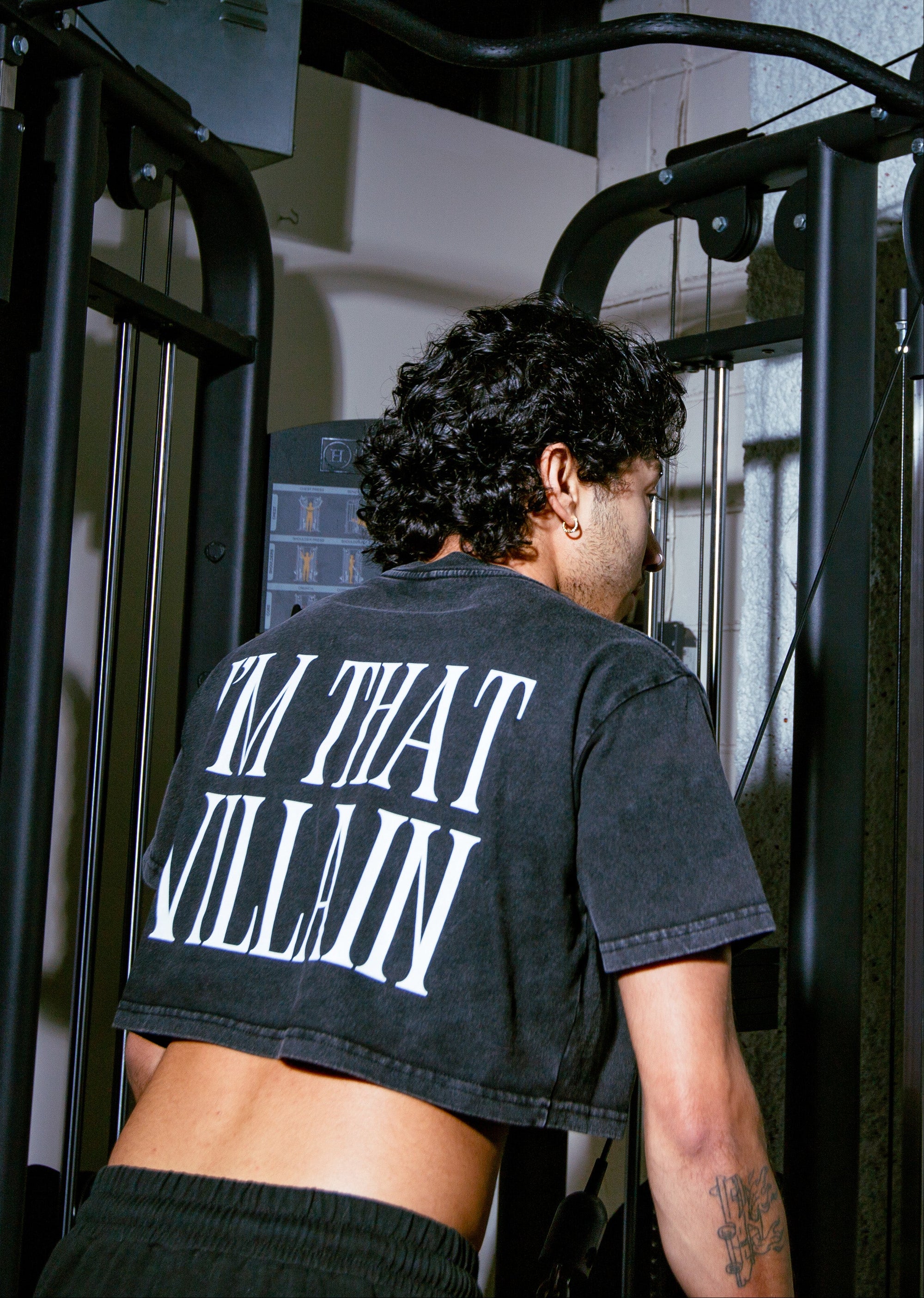 Trans person wearing a snow washed crop top with text "I'm that villain" in a gym setting