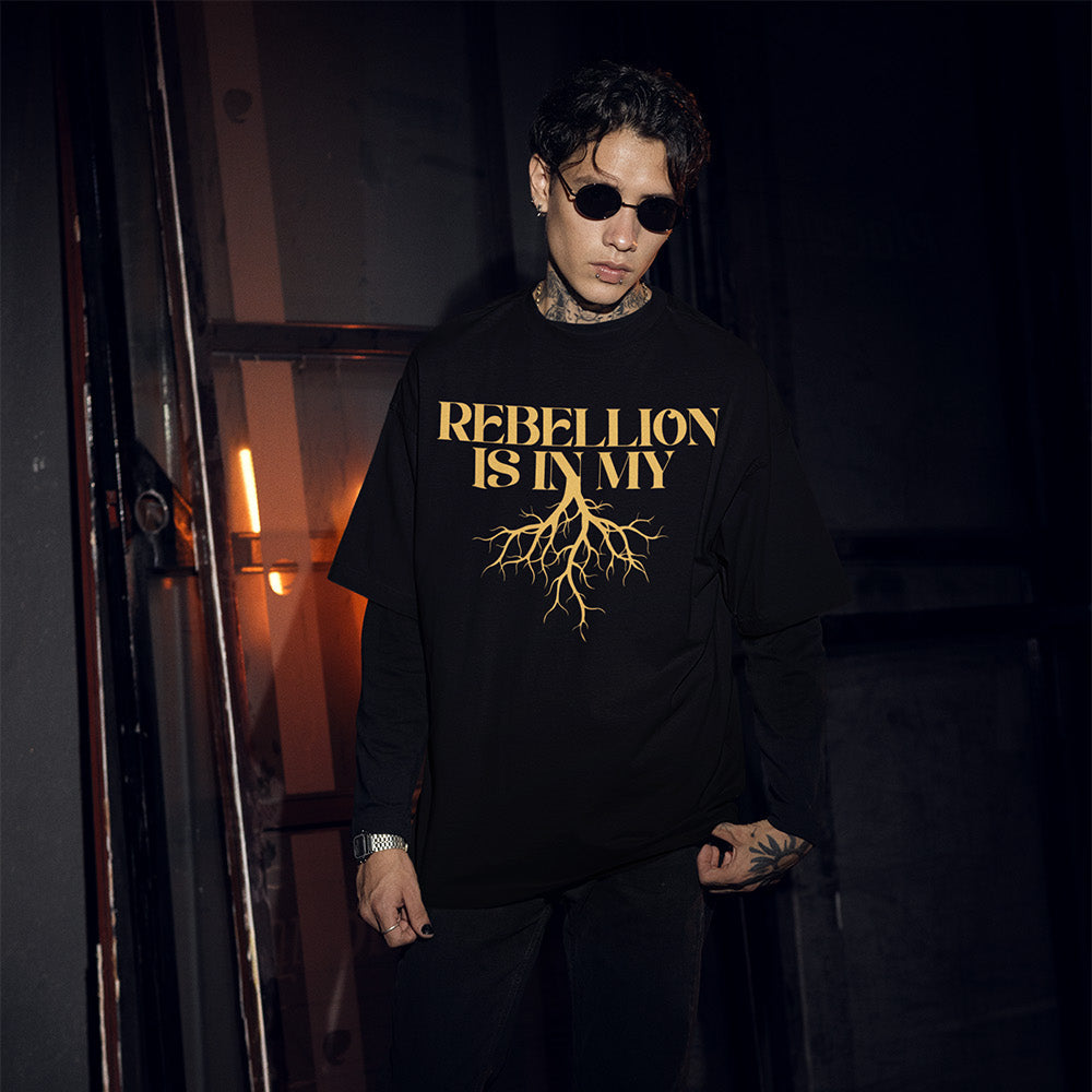 Person wearing a black sweatshirt with 'REBELLION IS MY ROOTS' text in gold, standing in a dimly lit room.